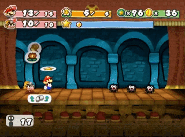 On a stage with an audience, Mario runs up to a fuzzy creature with crazy eyes, and slams it with a wooden mallet.